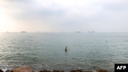 资料照片：在伊朗南部港口城市阿巴斯港外海，一名男子在海湾水域涉水，背景中可见船只正通过霍尔木兹海峡。（2026年9月7日）
