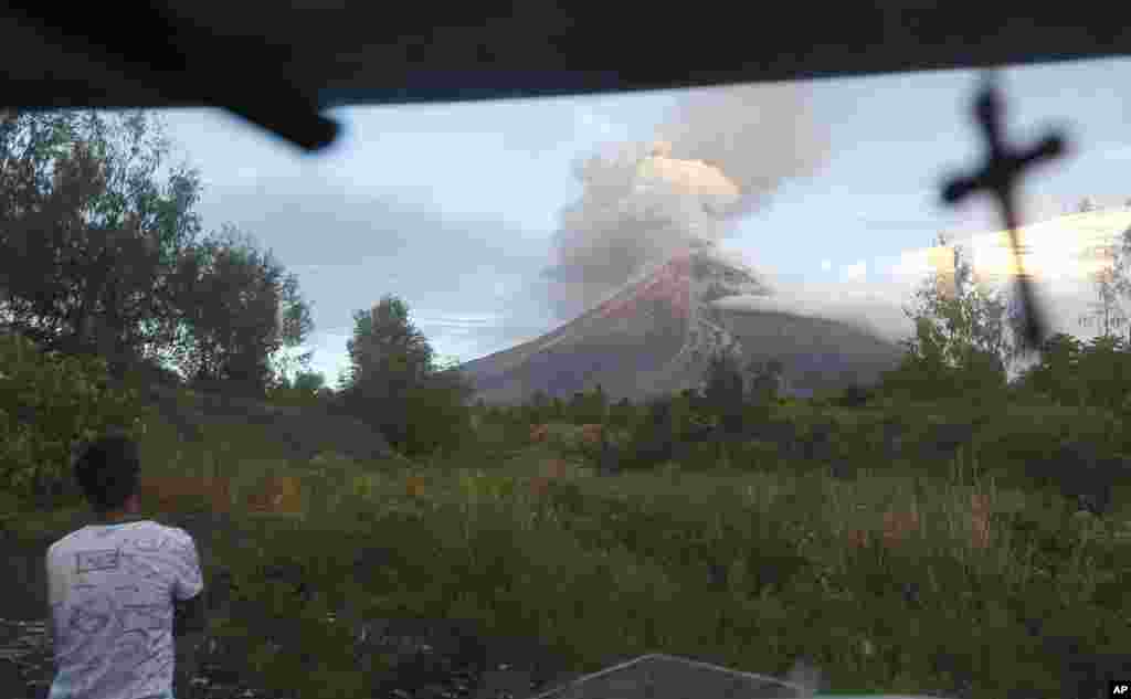 A public transport driver pauses, Jan. 25, 2018, to look at the erupting Mayon volcano behind a village in Legazpi city, Albay province, around 340 kilometers (200 miles) southeast of Manila, Philippines.