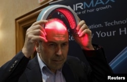 FILE - BBC television reporter Rory Cellan-Jones tries out a HairMax Laserband, a hands-free device described to treat hair loss and cause new hair growth, during the opening event at the Consumer Electronics Show in Las Vegas, Jan. 4, 2016.