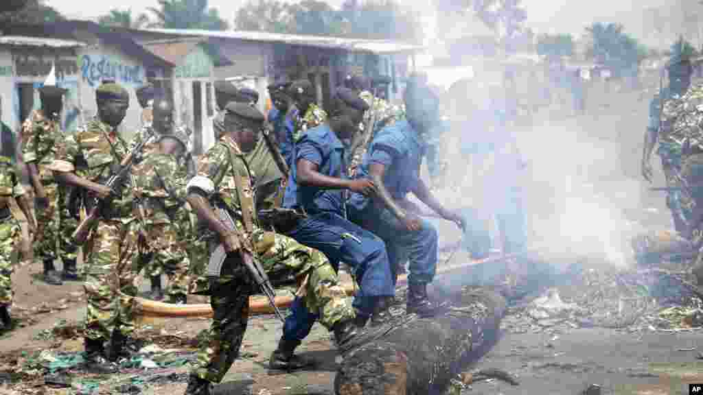 Des militaires et des policiers poussent de leurs pieds un tronc d'arbre pour dégager une barricade érigée par des manifestants ans le district de Cibitoke, à Bujumbura, Burundi, lundi 25 mai 2015