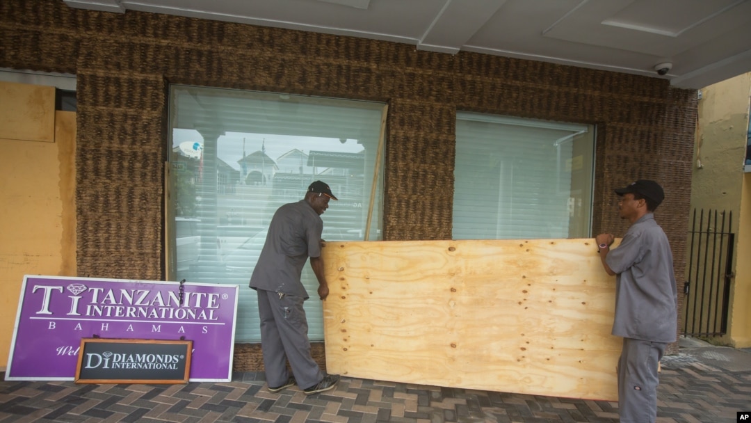 Two men carry a sheet of plywood as they cover the windows of the Diamond's International store, in preparation for the arrival of hurricane Joaquin in Nassau, Bahamas, Thursday, Oct. 1, 2015.