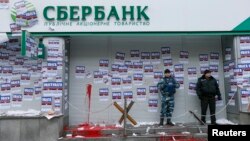 FILE - Security staff stand guard after a protest held by members of the Azov civil corps outside the central branch of Sberbank in Kyiv, Ukraine, Feb. 2, 2017. The stickers read in part: "Attention. This is a bank of the aggressor state."