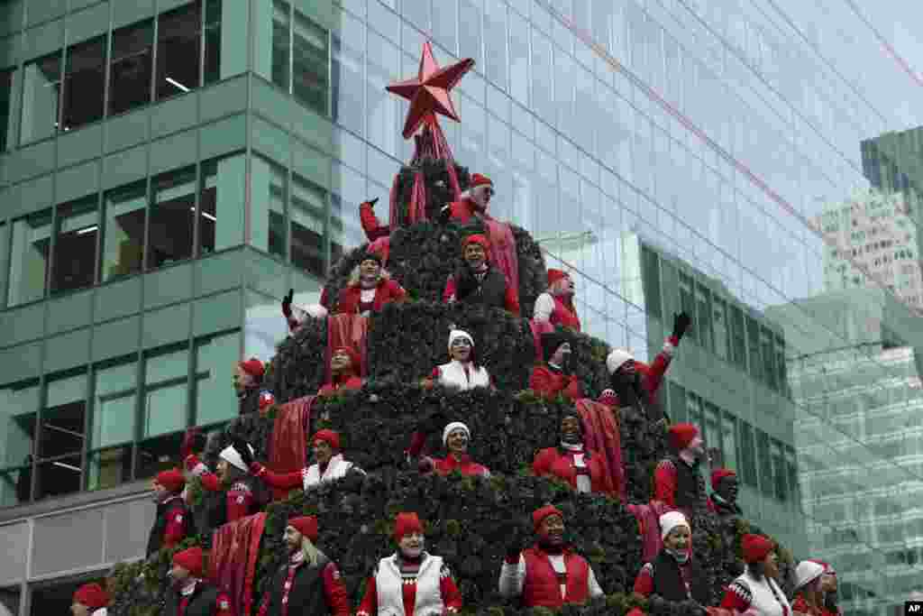 Carolers wave at spectators as they ride down Sixth Avenue in the Macy&#39;s Singing Christmas Tree float during the Macy&#39;s Thanksgiving Day Parade in New York.