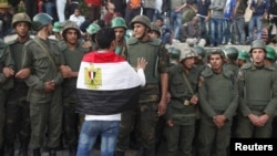 An anti-Mursi protester with an Egyptian flag around his shoulders talks to soldiers standing guard outside the Egyptian presidential palace in Cairo December 9, 2012.