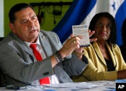 Francisco Portillo, left, president of the Honduran organization Francisco Morazan, holds up a postcard addressed to President Donald Trump asking him to extend Temporary Protected Status for tens of thousands of Central Americans and Haitians, as he and Marleine Bastien, right, executive director of Haitian Women of Miami, speak at a news conference in Miami, Florida, June 7, 2017.