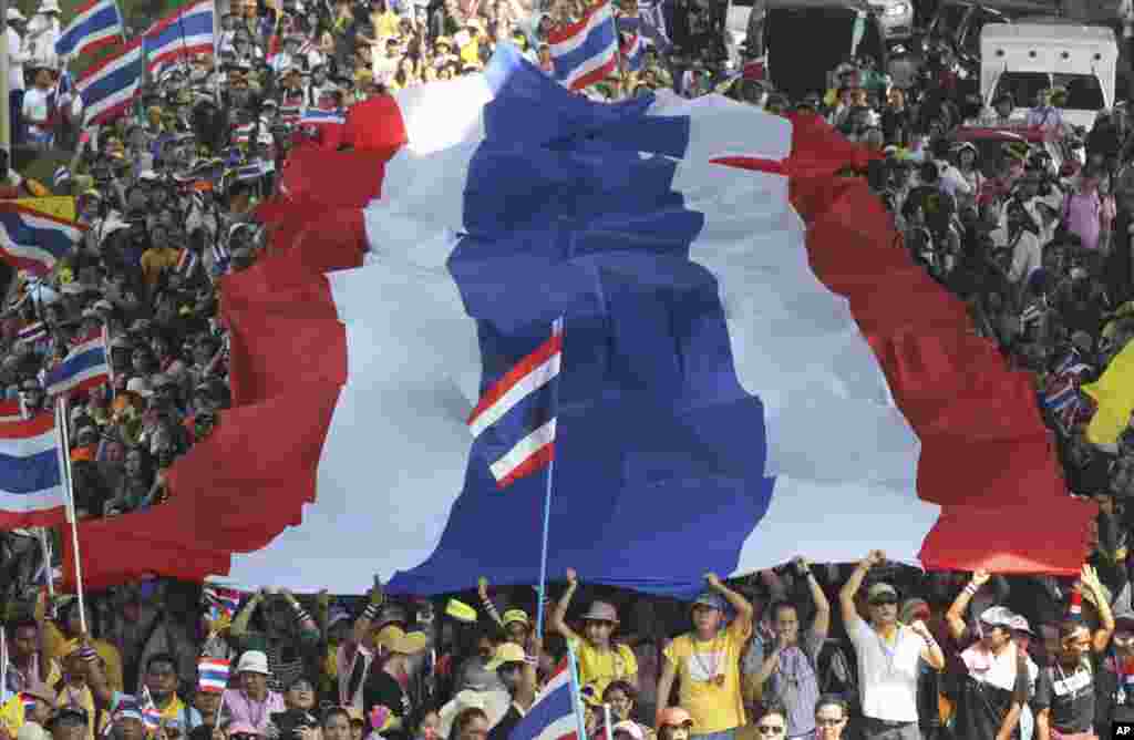Anti-government protesters carry a huge Thai national flag as they march in Bangkok. Thai Prime Minister Yingluck Shinawatra announced she will dissolve the lower house of Parliament and call elections in an attempt to calm the country&#39;s deepening political crisis.