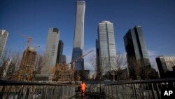 A cleaner walks on a pedestrian overpass against the skyscrapers under construction at the Central Business District in Beijing, Jan. 21, 2019. 