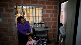 In this April 7, 2020, photo, Rosemary Paez Carabaja holds her daughter Laisa's hair as her son Leonardo enters to the room they rent in Buenos Aires, Argentina. (AP Photo/Natacha Pisarenko)