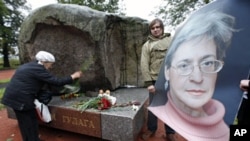 A 2009 file photo shows a man holding a portrait of killed journalist Anna Politkovskaya as a woman lays flowers during a commemorative rally in St.Petersburg