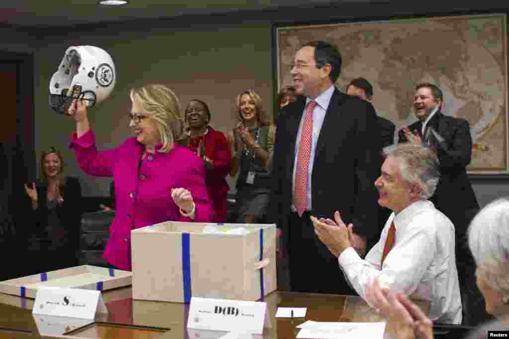 U.S. Secretary of State Hillary Clinton holds up a football helmet with the State Department logo on it, presented by Deputy Secretary of State Thomas Nides (C), who joked that 'Washington is a contact sport,' January 7, 2013. Clinton resumed her official duties, five days after being released from a hospital for treatment of a blood clot.