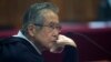 ARCHIVO - El encarcelado expresidente Alberto Fujimori, fotografiado a través de una ventana de vidrio, asiste a su juicio en una base policial en las afueras de Lima, Perú, el 28 de junio de 2016. 