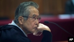 ARCHIVO - El encarcelado expresidente Alberto Fujimori, fotografiado a través de una ventana de vidrio, asiste a su juicio en una base policial en las afueras de Lima, Perú, el 28 de junio de 2016. 