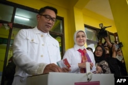 Ridwan Kamil (kiri), calon gubernur Jakarta, didampingi istrinya Atalia Praratya (tengah), memasukkan surat suara ke dalam kotak suara di tempat pemungutan suara untuk memilih dalam pemilihan kepala daerah serentak di Bandung, Jawa Barat, 27 November 2024. (TIMUR MATAHARI / AFP)