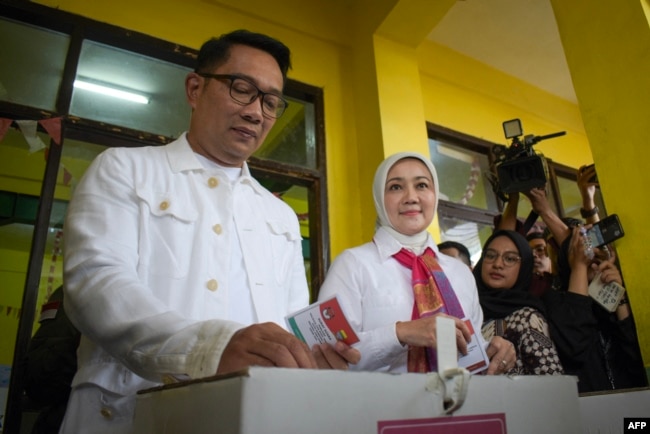 Ridwan Kamil (kiri), calon gubernur Jakarta, didampingi istrinya Atalia Praratya (tengah), memasukkan surat suara ke dalam kotak suara di tempat pemungutan suara untuk memilih dalam pemilihan kepala daerah serentak di Bandung, Jawa Barat, 27 November 2024. (TIMUR MATAHARI / AFP)