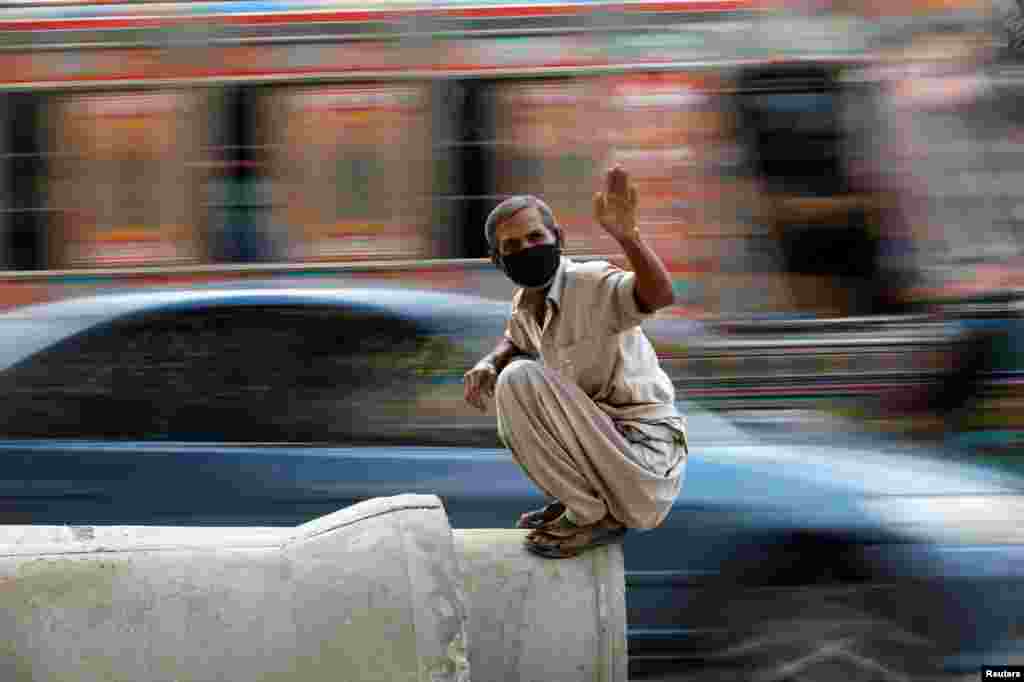 Vehicles move past a man wearing a protective mask against COVID-19 as he waits for the bus in Karachi, Pakistan.