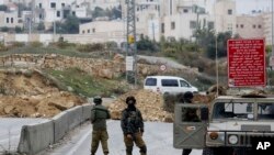 FILE - Israeli soldiers stand guard after the military blocked the road with an earth berm at one of the exits of the West Bank city of Hebron, Nov. 7, 2015.