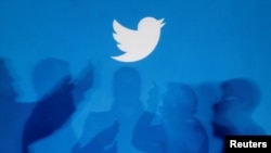 FILE: The shadows of people holding mobile phones are cast onto a backdrop projected with the Twitter logo in this illustration picture taken in Warsaw Sept.27, 2013