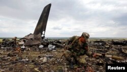 Seorang tentara separatis pro-Rusia mengumpulkan amunisi di dekat lokasi jatuhnya pesawat militer Ukraina Ilyushin-76 di Luhansk (14/6).