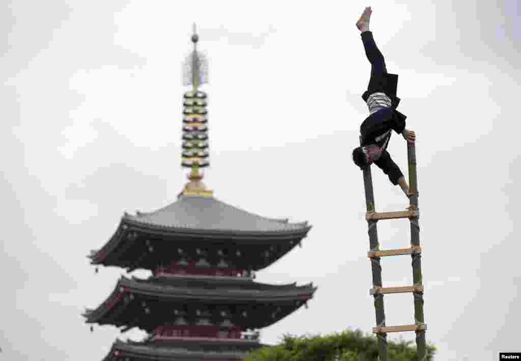 Men wearing traditional firefighter costumes perform acrobatic stunts atop a bamboo ladder following a memorial service for firefighters at Sensoji temple in Tokyo&#39;s downtown of Asakusa, Japan.