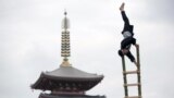 A man wearing a traditional firefighter costume performs acrobatic stunts atop a bamboo ladder following a memorial service for firefighters at Sensoji temple in Tokyo&#39;s downtown of Asakusa, Japan.