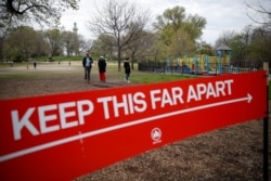 FILE - A sign by the New York City parks department indicates the appropriate measurement for social distancing as pedestrians linger in a field at Fort Greene Park, in New Yrok City, April 14, 2020.