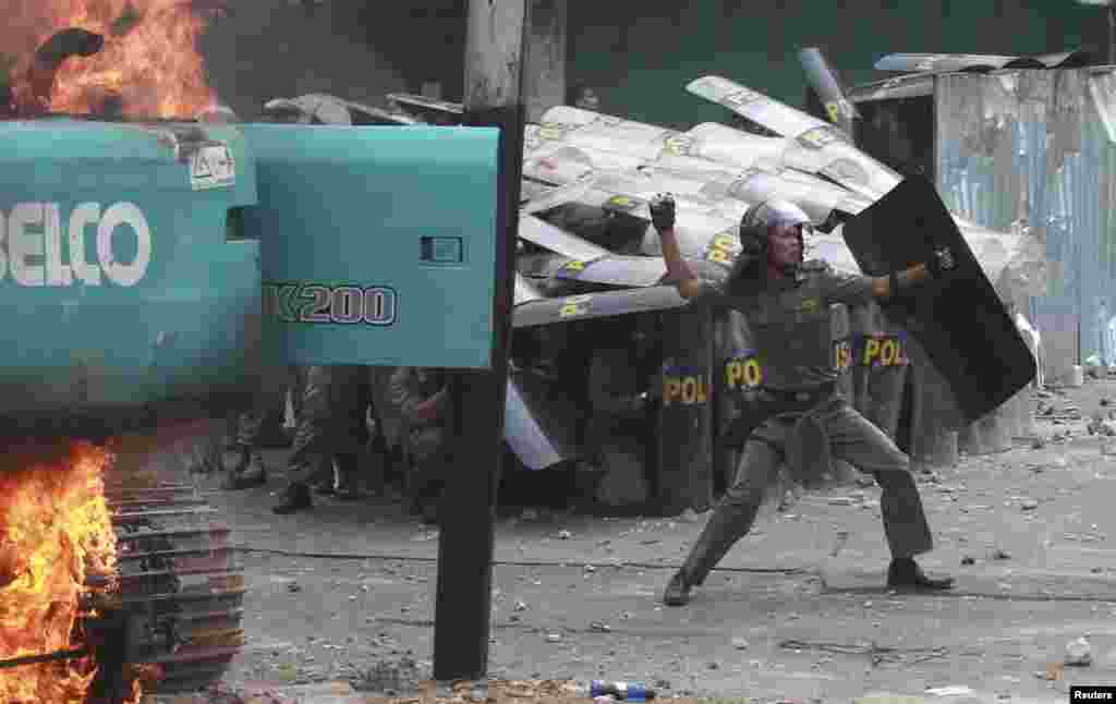 Petugas polisi kota melemparkan batu kembali ke arah warga yang berdemo di Kampung Pulo setelah bentrokan terjadi akibat penggusuran di Jakarta, Indonesia. (Foto: Antara Foto)