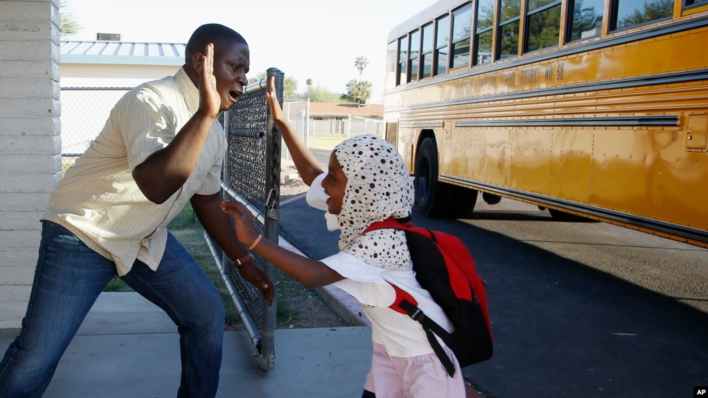 Samuel Lavi, left, a Congolese native who is a teaching assistant and family engagement liaison, greets first grader Kediga Ahmed as she arrives at the Valencia Newcomer School attend class, Oct. 17, 2019, in Phoenix. (AP Photo/Ross D. Franklin)