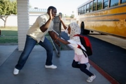 Samuel Lavi, left, a Congolese native who is a teaching assistant and family engagement liaison, greets first grader Kediga Ahmed as she arrives at the Valencia Newcomer School attend class Thursday, Oct. 17, 2019, in Phoenix. (AP Photo/Ross D. Franklin)