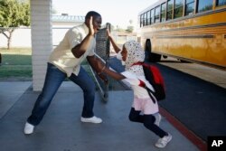 Samuel Lavi, left, a Congolese native who is a teaching assistant and family engagement liaison, greets first grader Kediga Ahmed as she arrives at the Valencia Newcomer School attend class Thursday, Oct. 17, 2019, in Phoenix. (AP Photo/Ross D. Franklin)