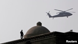 FILE - An Afghan security guard keeps watch on the roof of a building as a NATO helicopter flies overhead in Kabul.