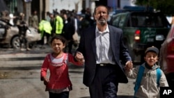 Seorang pria Afghanistan membawa anak-anaknya pergi dari tempat bom bunuh diri yang menyerang konvoi NATO di Kabul, Afghanistan (16/5). (AP/Anja Niedringhaus)