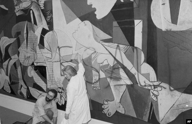 FILE - Museum of Modern Art employees clean paint off of Pablo Picasso's mural "Guernica", Feb. 28, 1974, after a 30-year-old man spray painted the words "kill lies all." Minutes after the man defaced the painting, the paint was removed and museum officia