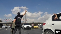 This UGC image posted on Twitter on Nov. 3, 2022, shows a person, wearing a shirt which translates from Persian to "We will fight, we will die, we will take back Iran," gesturing in the middle of a busy highway in the city of Karaj in the northern Alborz Province.