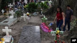 A couple walks next to one of the graves of gang members whose tombstone was destroyed on order of the government, during the Day of the Dead at the Nueva San Salvador Cemetery, in Santa Tecla, El Salvador, Nov. 2, 2022. 