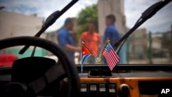 ARCHIVO - Una bandera cubana y una estadounidense cuelgan del parabrisas de un automóvil estacionado en un garaje en La Habana, Cuba, en agosto de 2016. 