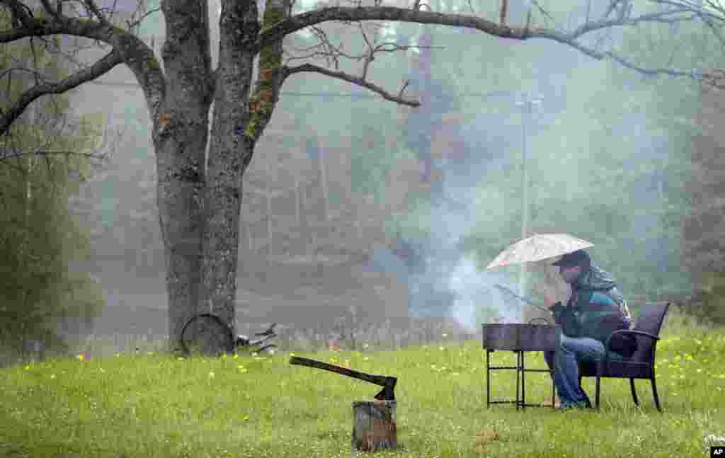 A holidaymaker barbeques under an umbrella during a rainy day at the lake in Ignalina region, some 106 km (66 miles) north of the capital Vilnius, Lithuania.