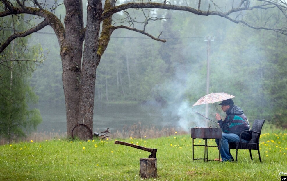 A holidaymaker barbeques under an umbrella during a rainy day at the lake in Ignalina region, some 106 km (66 miles) north of the capital Vilnius, Lithuania.