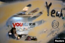 FILE - An employee is seen through a glass wall as she walks past the logo of Youku.com above the reception desk at the company's headquarters in Beijing, Dec. 9, 2010.