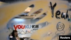 បុគ្គលិក​ម្នាក់​ដើរកាត់​ស្លាក​របស់​គេហទំព័រ Youku.com ពី​លើ​តុ​ទទួលភ្ញៀវ​នៅ​ឯ​ក្រុមហ៊ុន​នោះ​នៅ​ក្រុង​ប៉េកាំង កាល​ពី​ថ្ងៃ​ទី០៩ ខែ​ធ្នូ ឆ្នាំ​២០១០។