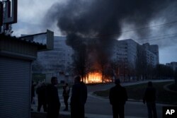 Residents stand outside their apartments as shops burn after a Russian attack in Kharkiv, Ukraine, April 11, 2022.