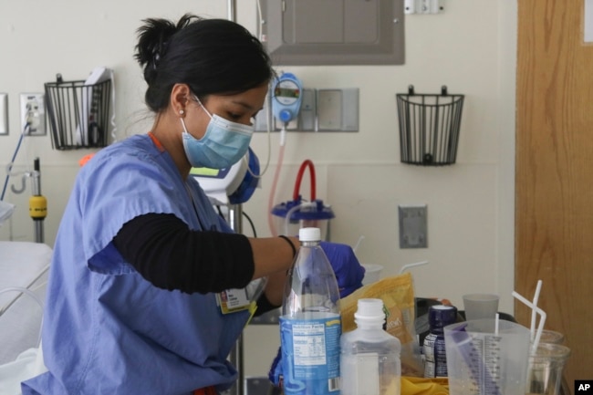 In this image provided by the U.S. Army, U.S. Air Force 1st Lt. Mary Coleman, a nurse assigned to a military medical team, prepares a patient's medication while supporting the COVID-19 response operations at University of Rochester Medical Center in Rochester, N.Y., March 5, 2022. (Spc. Khalan Moore/U.S. Army via AP)