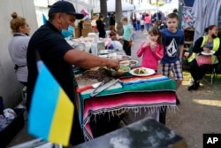 Mexican volunteer Felix Lara prepares tacos for Ukrainians refugees at a makeshift camp near the border, Monday, April 4, 2022, in Tijuana, Mexico. (AP Photo/Gregory Bull)