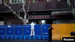2022年4月11日，在中国上海为遏制新冠疫情(COVID-19)传播而实施封锁期间，一名身穿防护服的人正在查看封闭区域周围的路障。