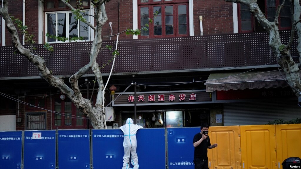 2022年4月11日，在中国上海为遏制新冠疫情(COVID-19)传播而实施封锁期间，一名身穿防护服的人正在查看封闭区域周围的路障。(photo:VOA)