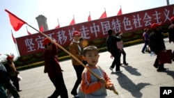 资料照：一个男孩手举红旗走过天安门广场上竖立的走中国特色社会主义道路的标语牌。（2007年10月9日）