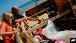 FILE - Tom and Andrea Heinz investigate the motor of a beached migrant boat on Coco Plum Beach in Marathon, Fla., Jan. 19, 2023.