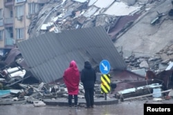 People stand in front of a collapsed building after an earthquake in Kahramanmaras, Turkey, Feb. 6, 2023.