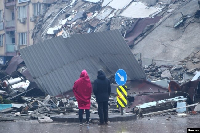 People stand in front of a collapsed building after an earthquake in Kahramanmaras, Turkey, Feb. 6, 2023.