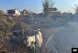 Warga menyaksikan puing-puing pesawat saat tim penyelamat memeriksa sekitar lokasi kecelakaan, di Pokhara, Nepal, Minggu, 15 Januari 2023. (AP/Krishna Mani Baral)