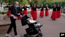 资料照：一名老年妇女推着一个婴儿走过北京一所公园里跳广场舞的妇女。（2021年10月14日）